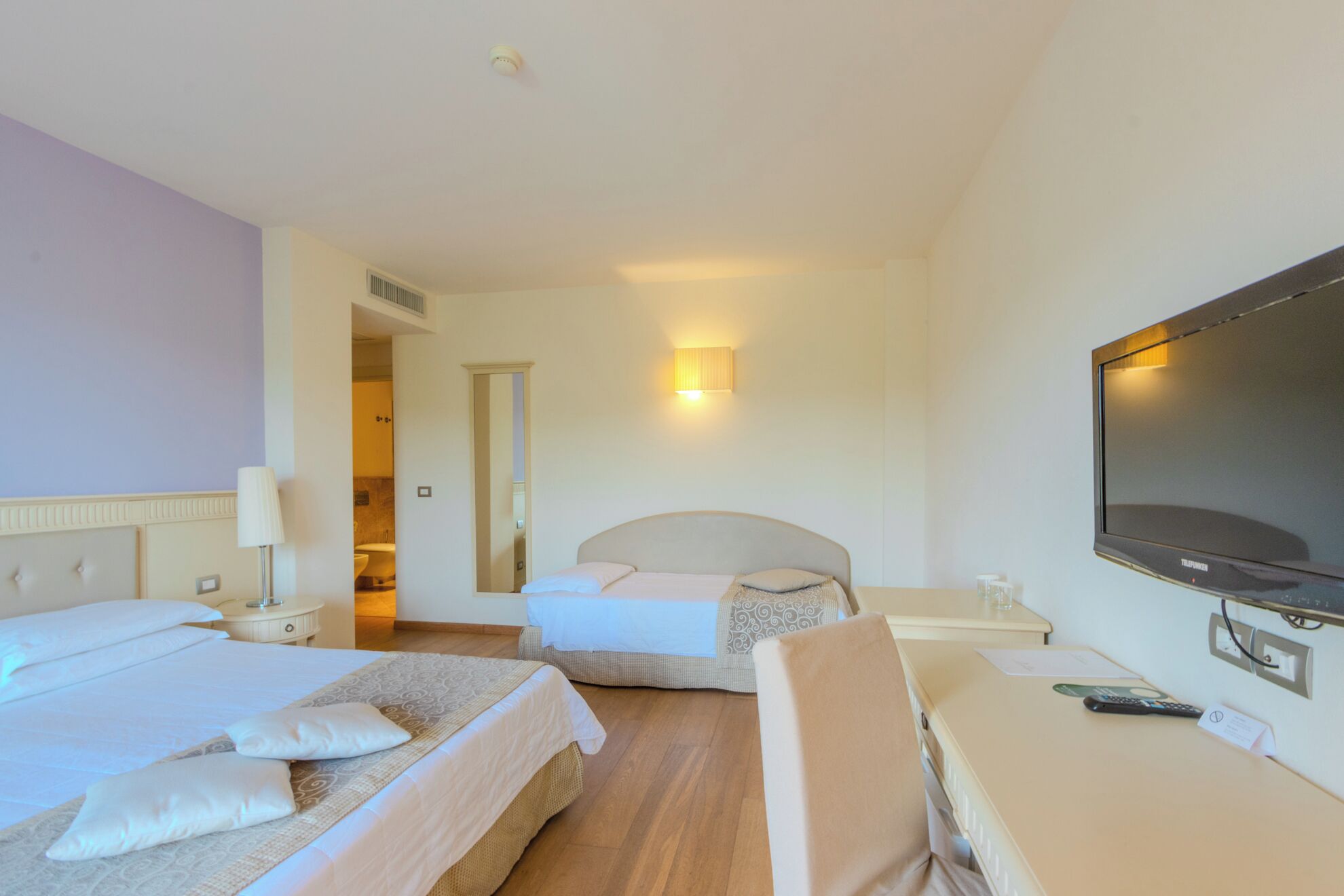 A hotel room with two beds, a TV, a bedside table, a lamp, and a mirror.