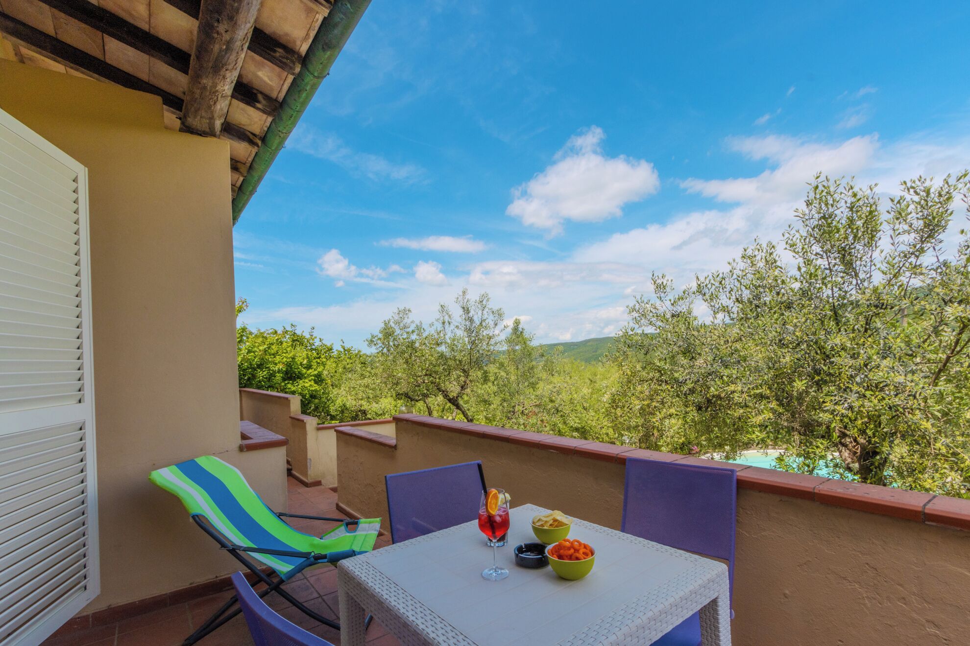A balcony with a table, chairs, and a view of trees.