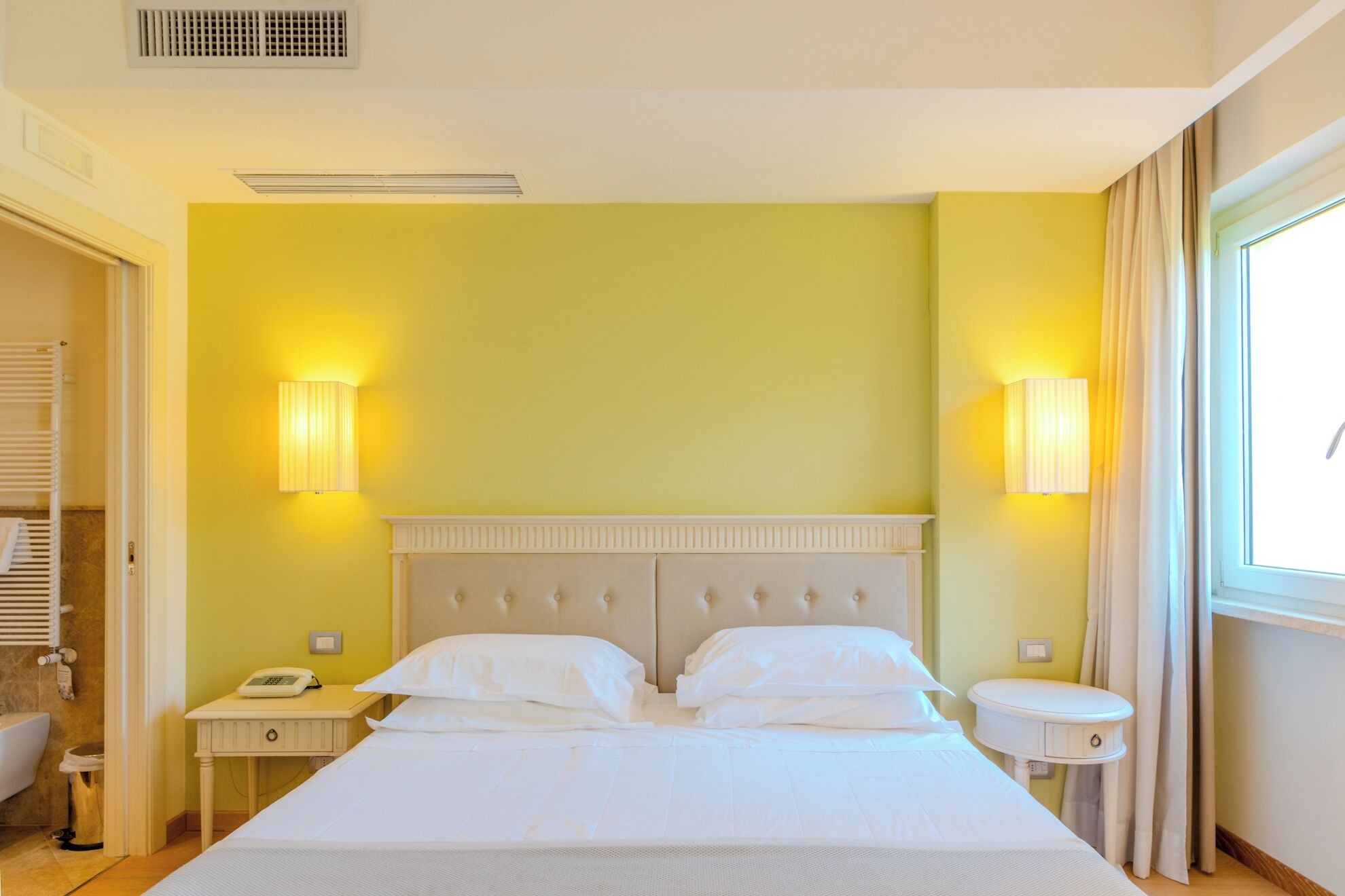 Una camera d'albergo con un letto, comodini, un telefono e una finestra con tende.