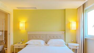 Una camera d'albergo con un letto, comodini, un telefono e una finestra con tende.