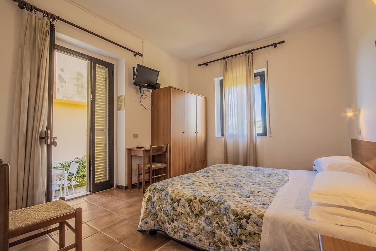 Une chambre à coucher comprenant un lit, un bureau, une chaise, une armoire, un téléviseur et un balcon.