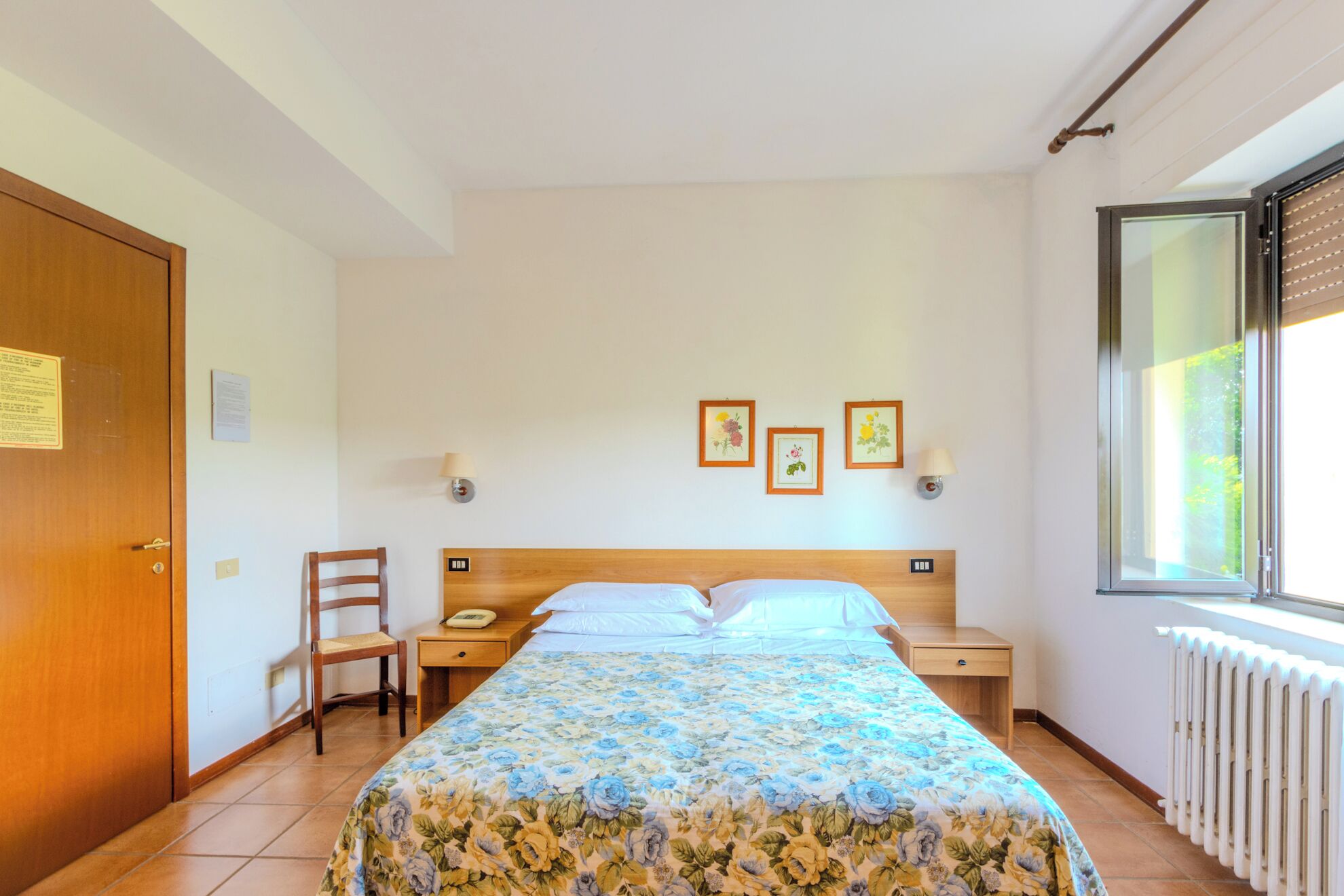 Um quarto com cama, cadeira, mesa de cabeceira, janela e radiador.