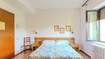 Um quarto com cama, cadeira, mesa de cabeceira, janela e radiador.