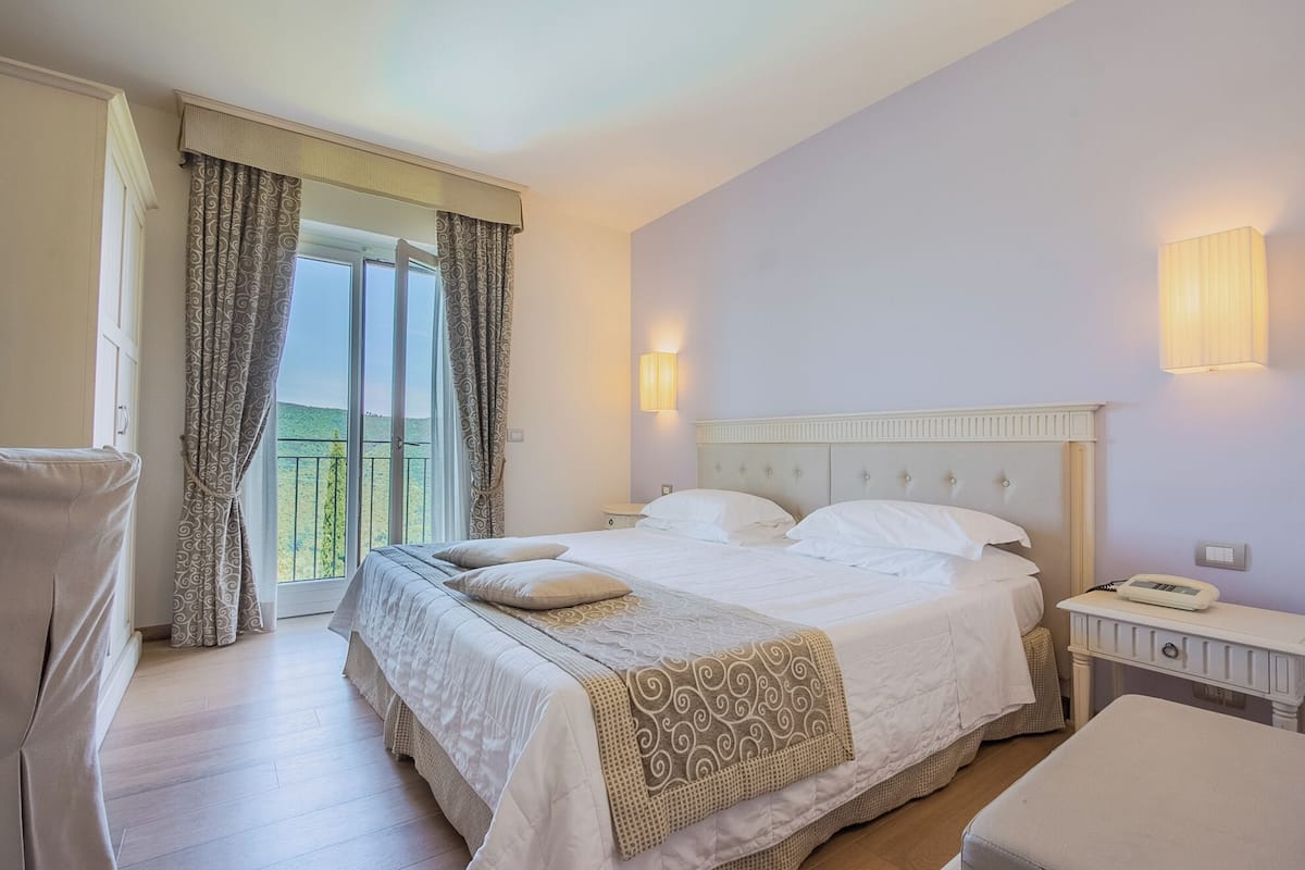 Une chambre d’hôtel avec un lit, une chaise, une table de chevet et une vue par une fenêtre avec des rideaux.
