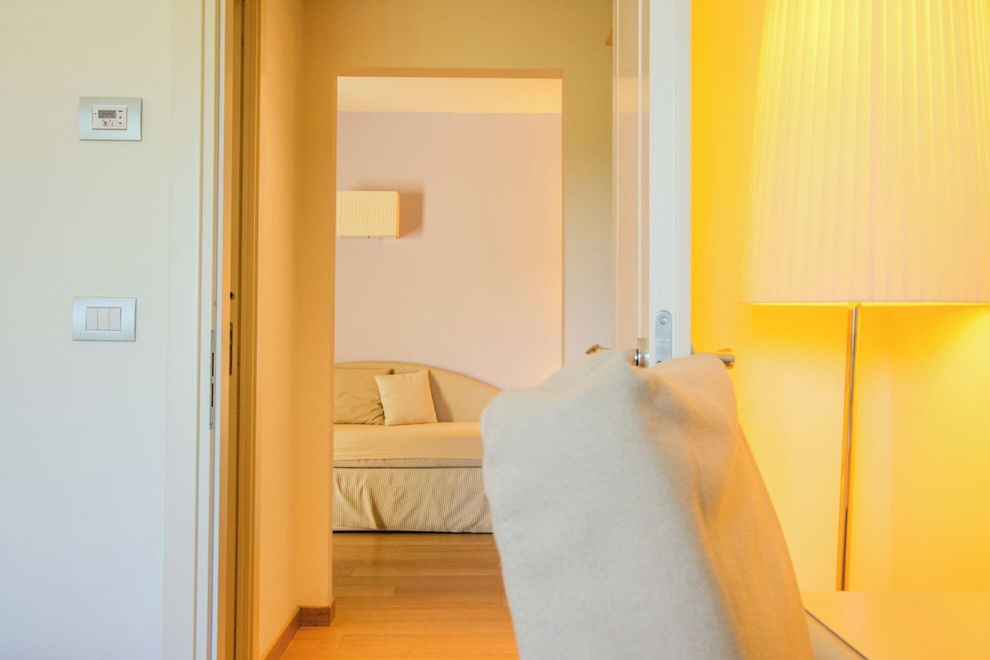 A hallway leading to a bedroom with a bed, a bedside table, and a lamp.
