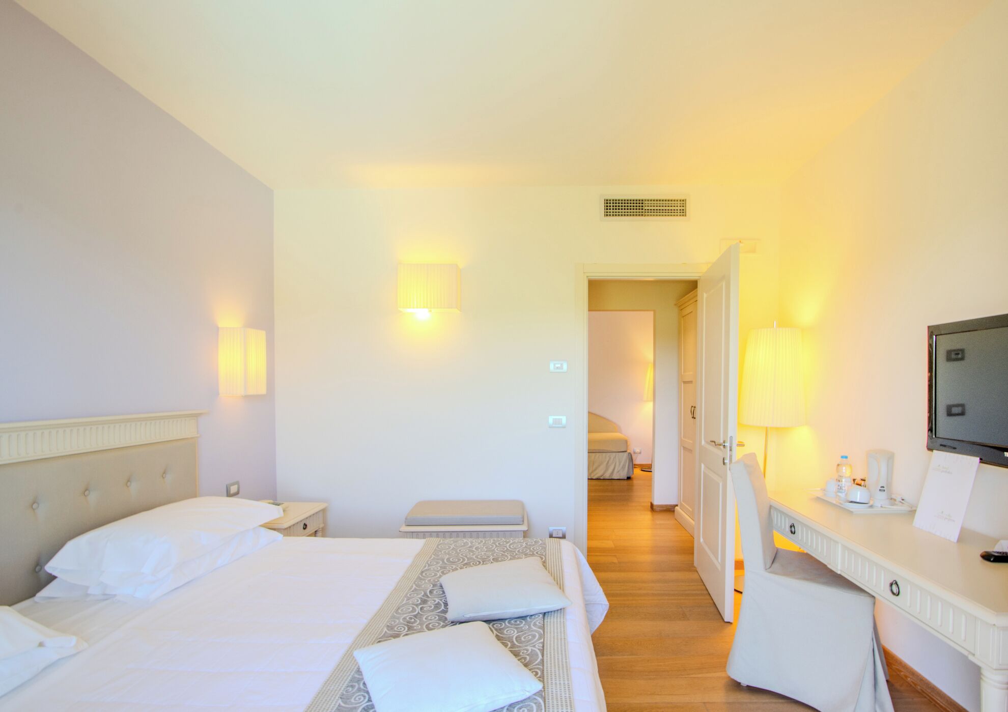 Habitación de hotel con dos camas, un escritorio, una silla, un televisor y un baño visible al fondo.