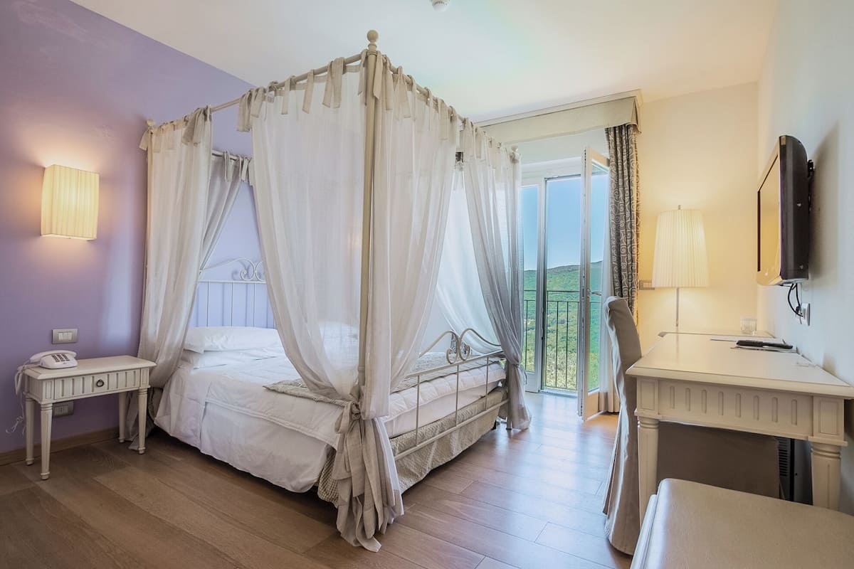 Une chambre à coucher avec un lit à baldaquin, une table de chevet avec une lampe, un bureau avec une chaise et un téléviseur.