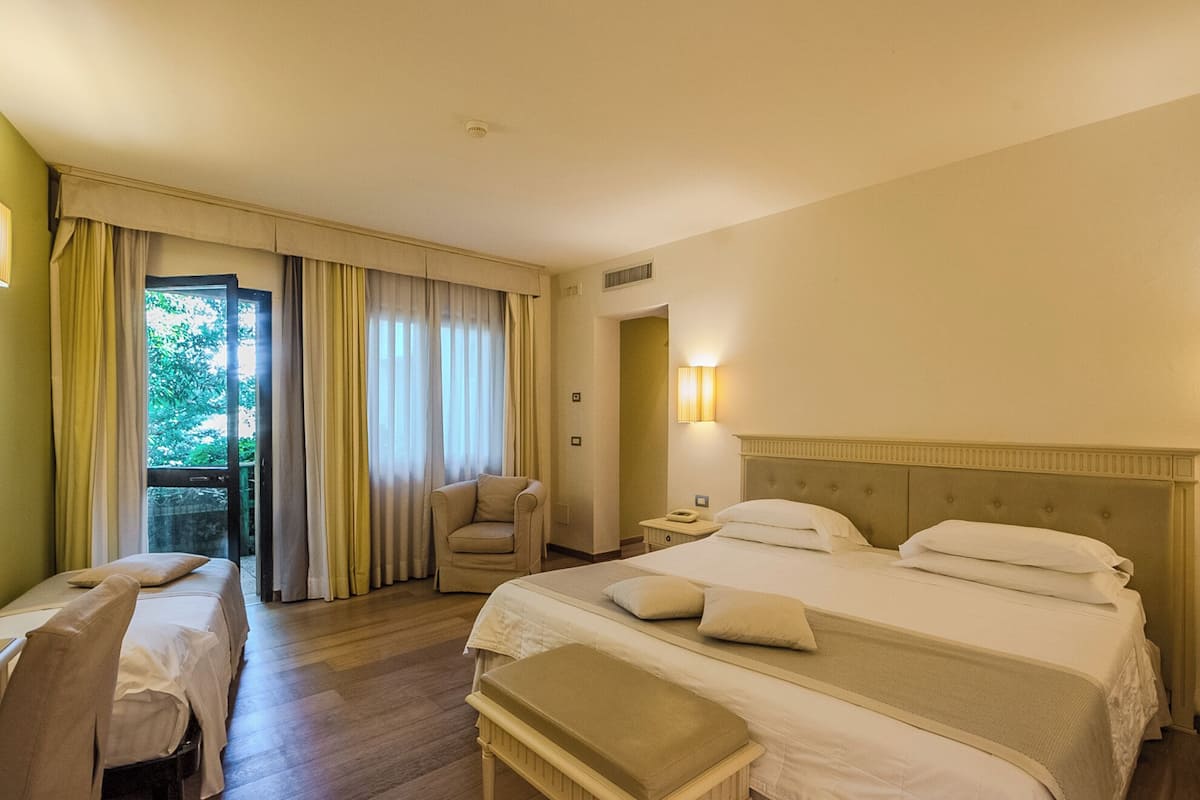 Une chambre d’hôtel avec un lit, une chaise, un bureau et un balcon avec des rideaux.