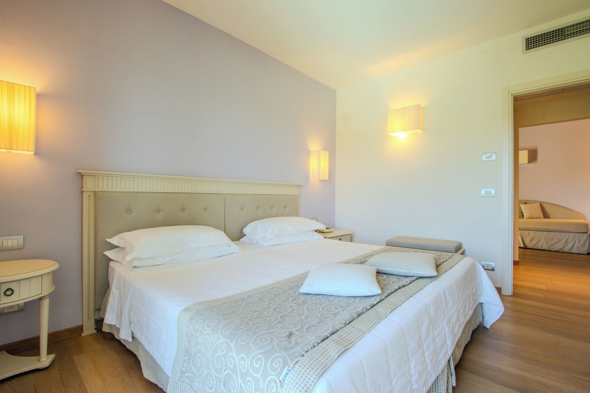 A hotel room with a large bed, bedside tables, and wall-mounted lamps.