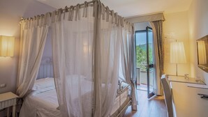 Une chambre à coucher avec un lit à baldaquin, un bureau et une vue sur la verdure environnante.