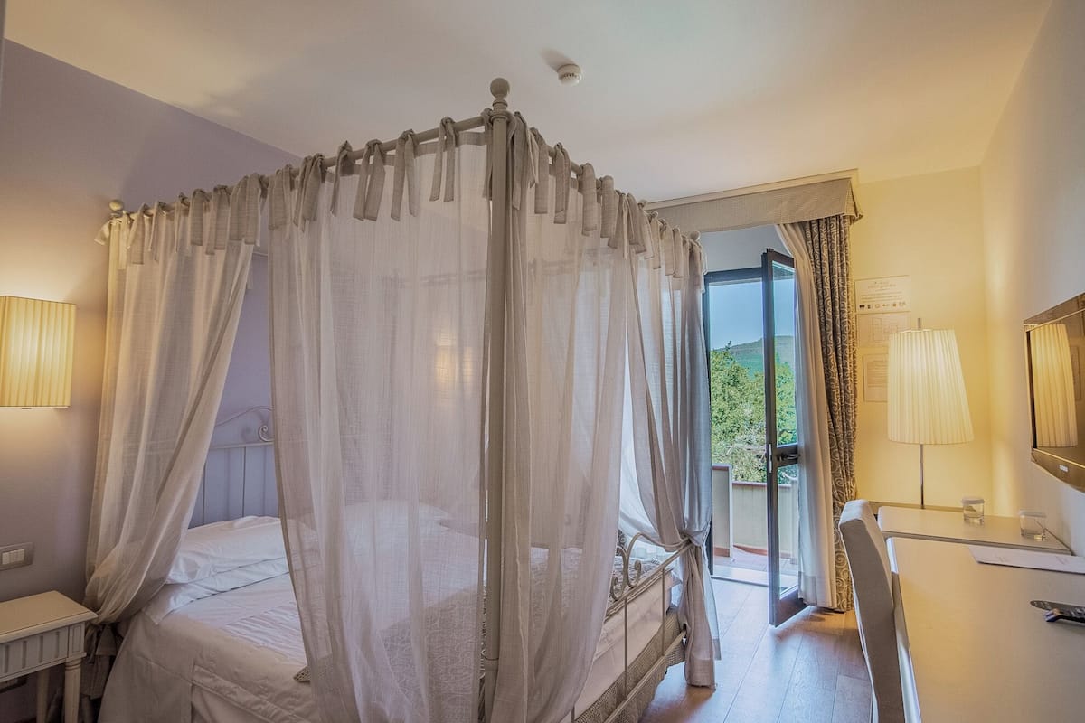 Une chambre à coucher avec un lit à baldaquin, un bureau et une vue sur la verdure environnante.