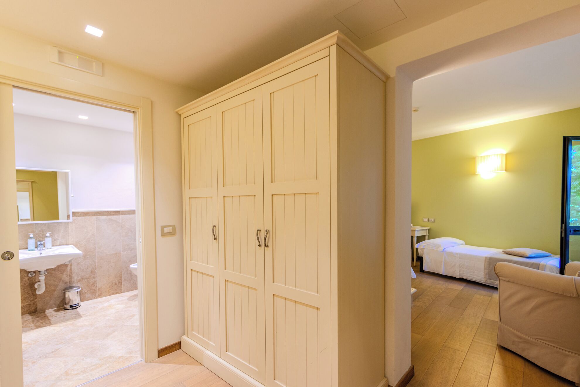 Une chambre d’hôtel avec un grand placard, une salle de bain avec un lavabo et un lit avec une table de chevet.