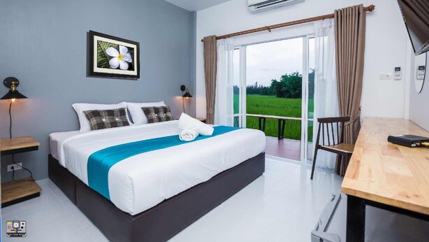 A modern bedroom with a large bed, a desk, and a view of a green landscape through the window.