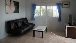 A living room with a leather sofa, a coffee table, a TV, and a window with curtains.