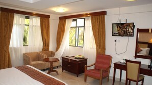 Ein Hotelzimmer mit einem Bett, zwei Sesseln, einem kleinen Tisch, einem Schminktisch und einem an der Wand befestigten Fernseher.