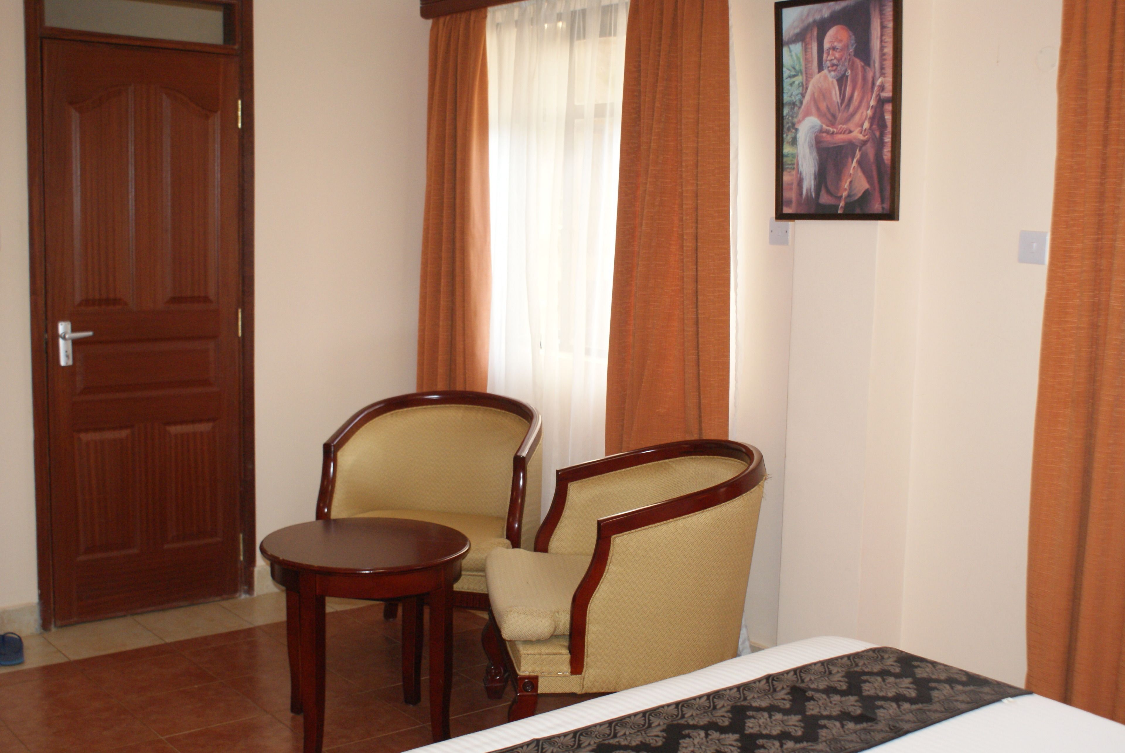 Habitación de hotel con puerta de madera, dos sillones, una mesita y una cama con colcha estampada.