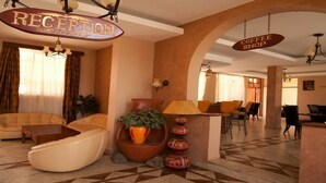 Ein Hotel-Empfangsbereich mit Empfangstresen, einem Coffeeshop-Schild und einer Sitzecke mit Sofas und einem Blumentopf.