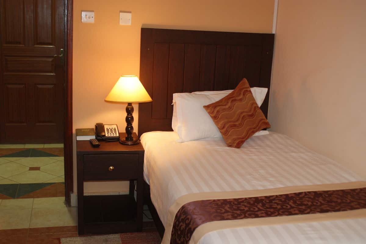 Une chambre d’hôtel avec un lit, une table de chevet avec une lampe, un téléphone et un plaid à motifs.