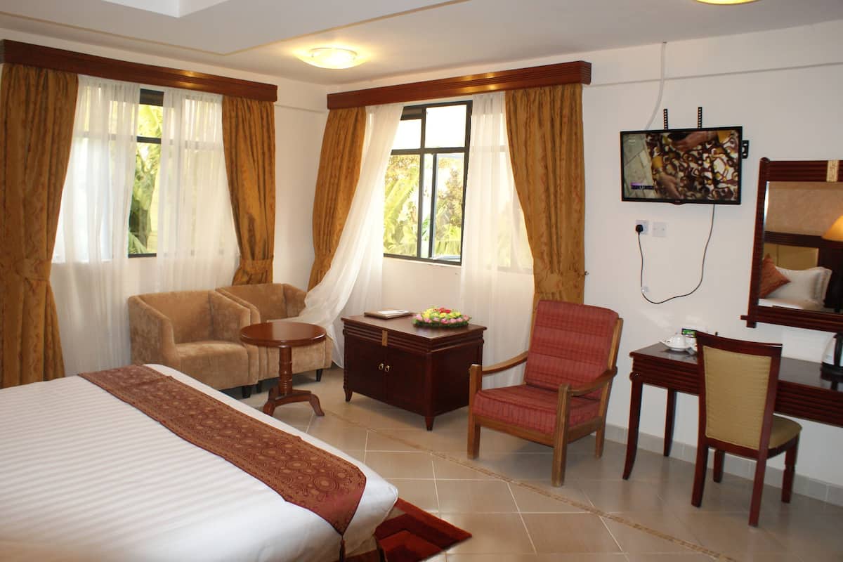 Une chambre d’hôtel comprenant un lit, deux fauteuils, une petite table, un meuble et un téléviseur.
