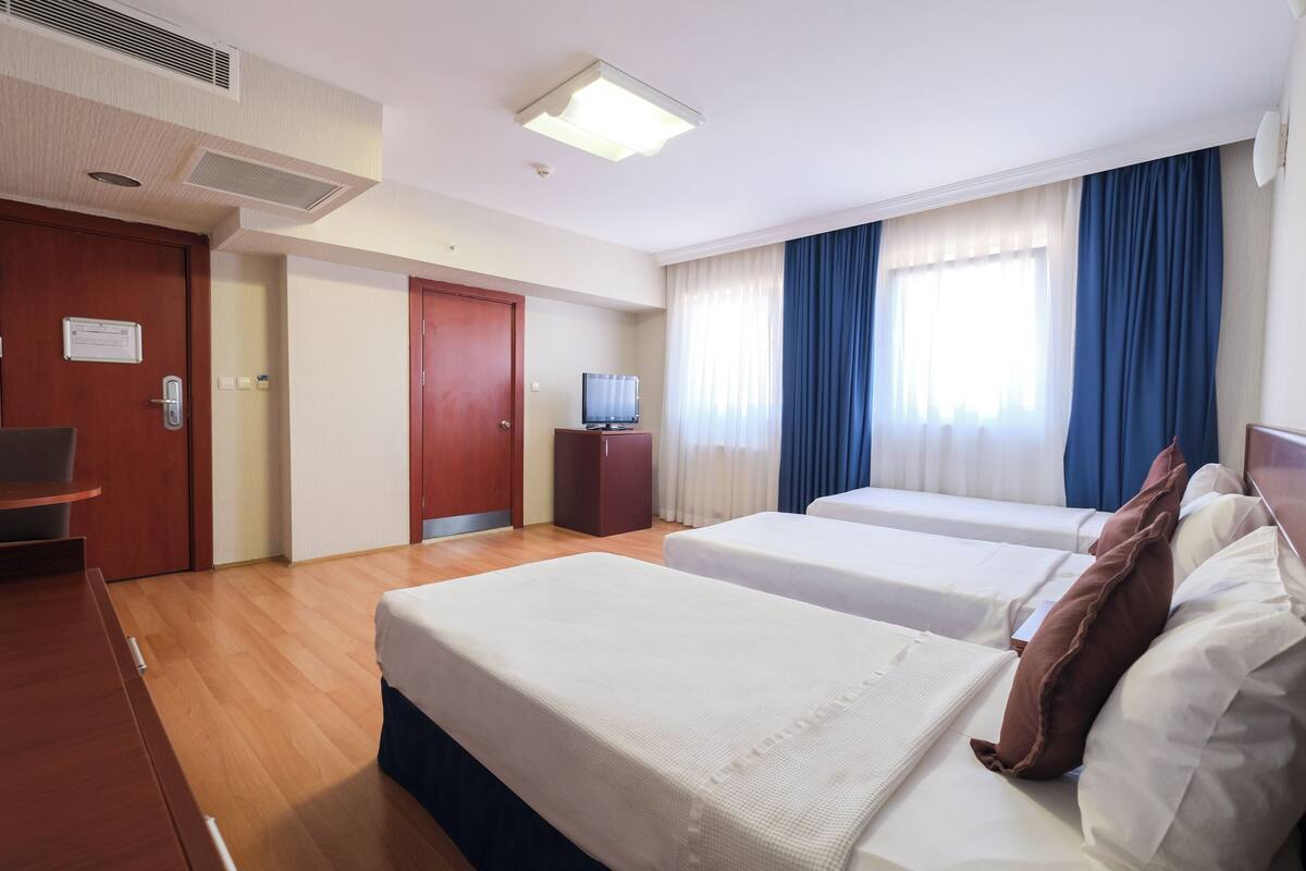 A hotel room with two beds, a desk, a television, and a door with a sign.