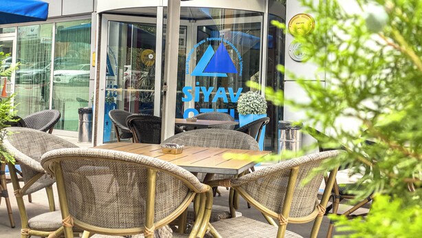 An outdoor seating area with wicker chairs and a table, a blue awning, and a glass door with signage. - Siyav Hotel (Ankara)