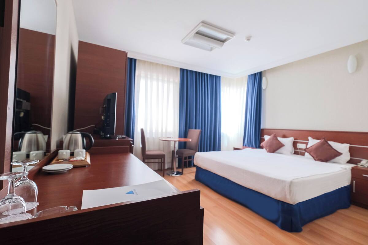 A hotel room with a large bed, a desk with a chair, a coffee machine, and a TV.