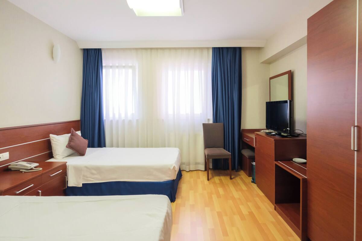 A hotel room with two beds, a desk with a chair, a television, and a wardrobe.
