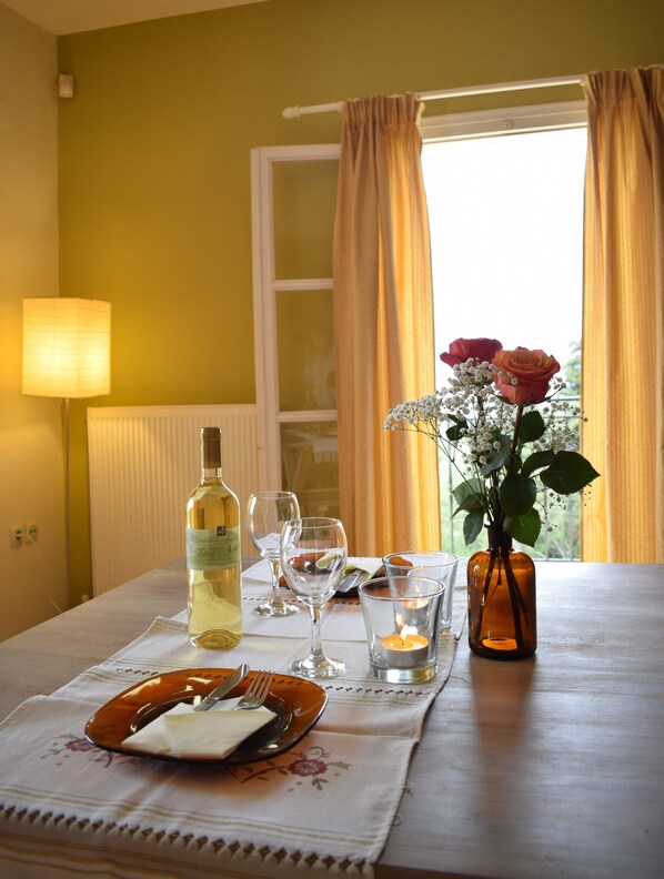 Una mesa de comedor dispuesta con una botella de vino, copas, una vela y un florero con flores.