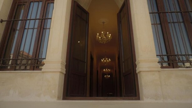 A building entrance with a large open doorway, a chandelier, and a view into a corridor with multiple doors. - La PLace Hotel (Zahlé)