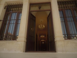 A building entrance with a large open doorway, a chandelier, and a view into a corridor with multiple doors. - La PLace Hotel (Zahlé)