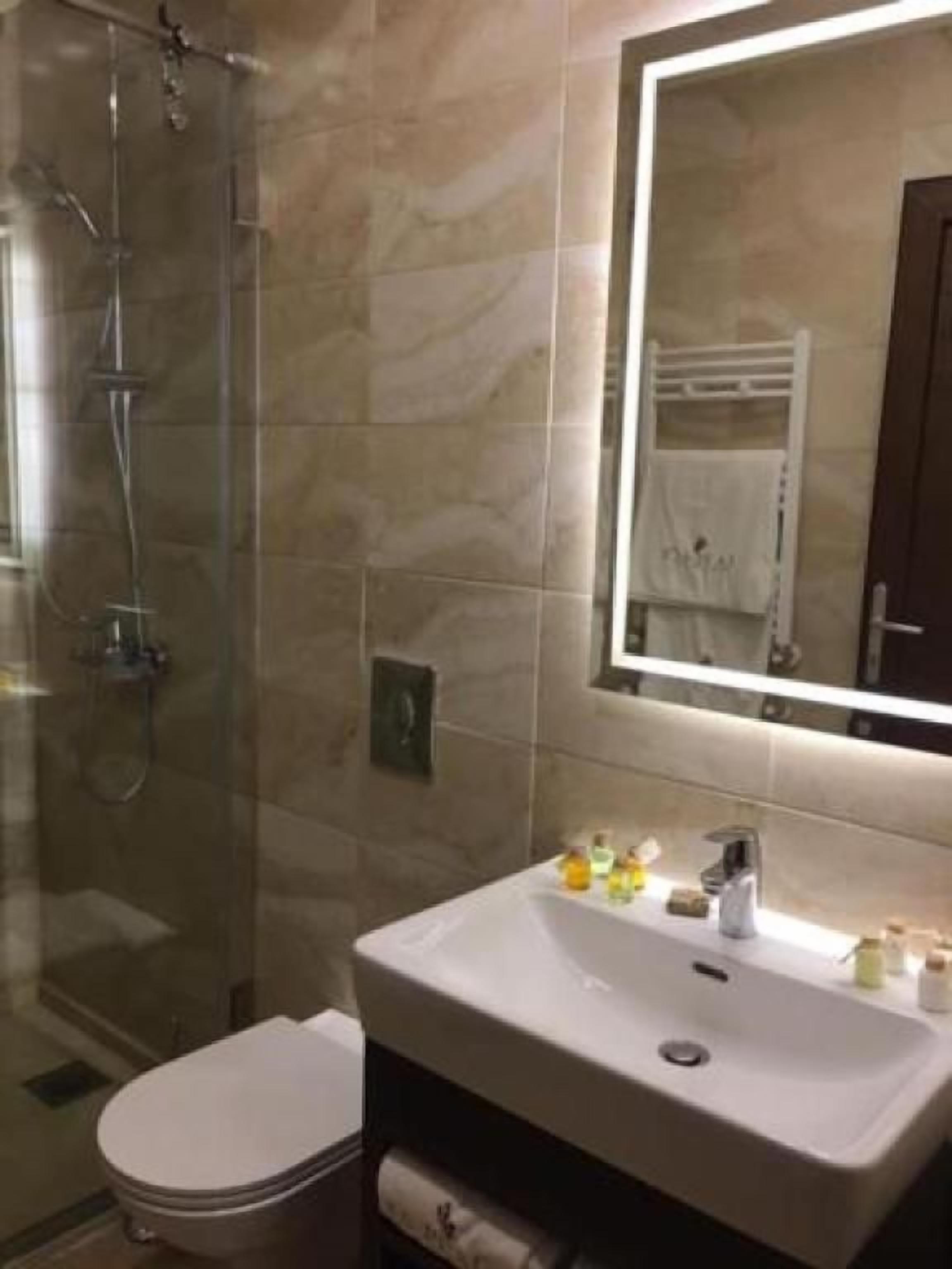 A bathroom with a glass shower enclosure, a white sink with a mirror above it, and a towel rack.