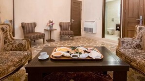 A room with two ornate sofas, a coffee table with a tray of food, a chandelier, and a patterned rug. - La PLace Hotel (Zahlé)