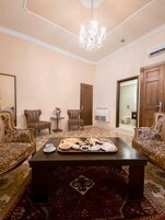 A room with two ornate sofas, a coffee table with a tray of food, a chandelier, and a patterned rug.