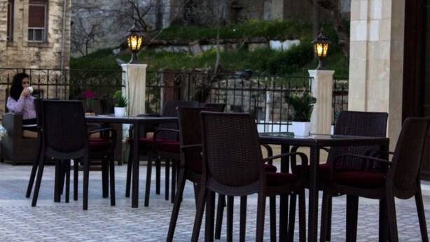 An outdoor cafe with wicker chairs and tables, stone walls, and decorative lanterns. - La PLace Hotel (Zahlé)