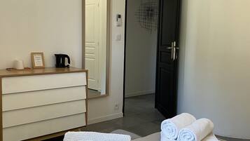 A hotel room with a bed, a dresser, a mirror, a door, and a wall-mounted light switch.