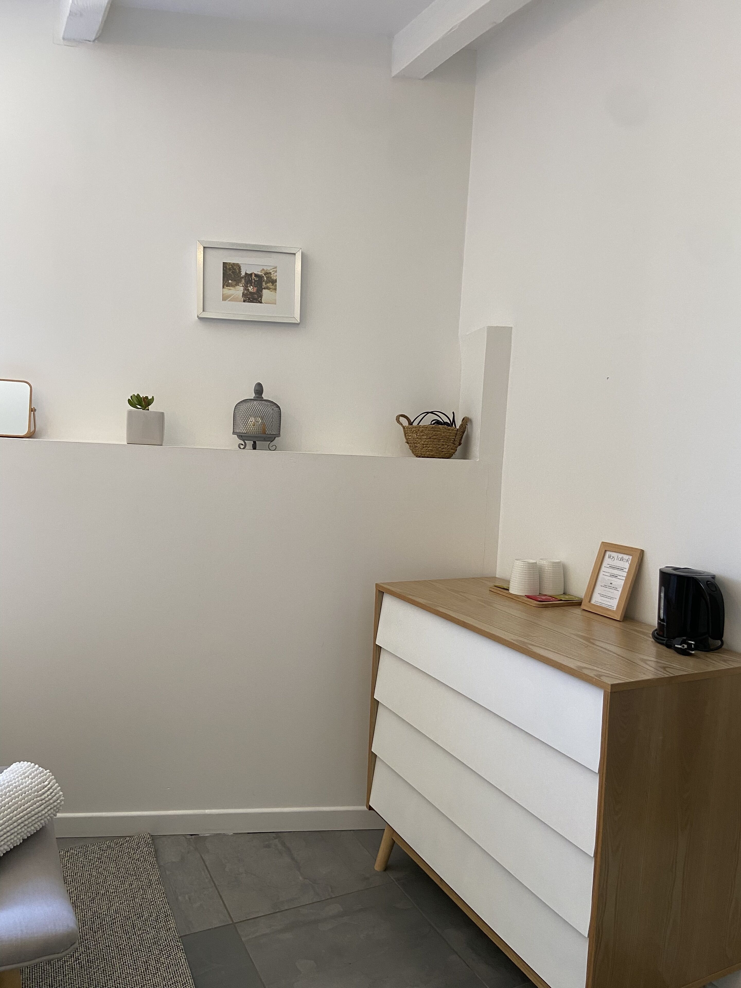 Una habitación limpia y minimalista con un escritorio de madera, una pequeña planta en maceta, un cuadro enmarco y una cafetera.