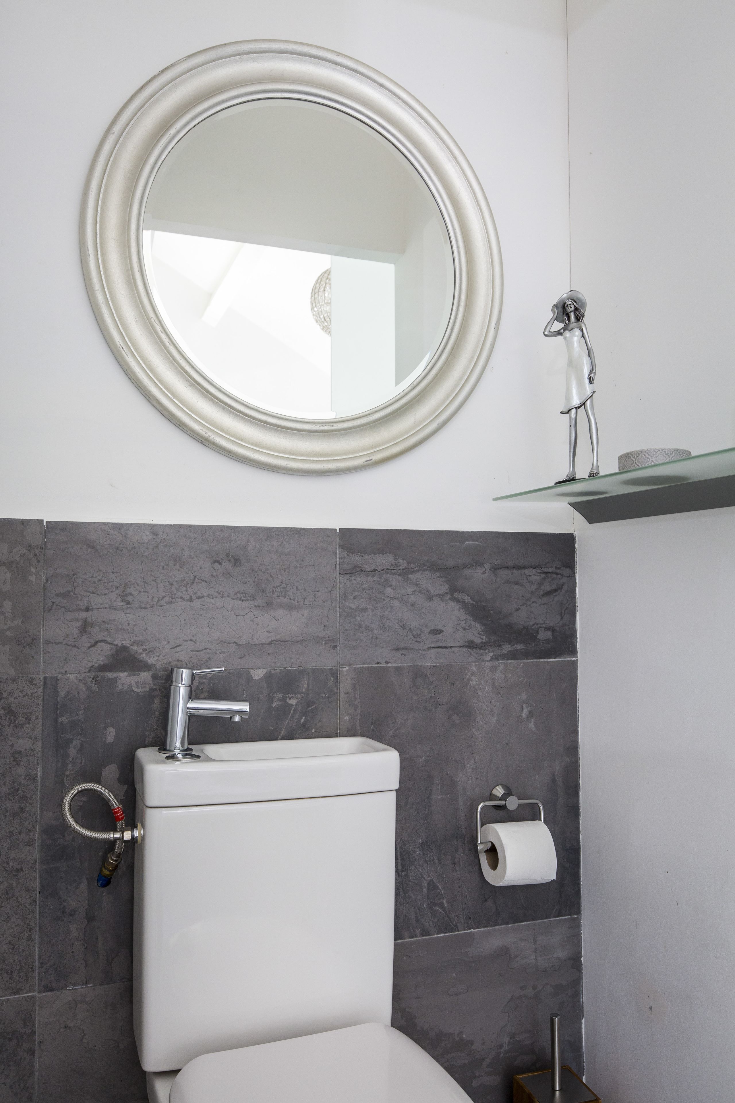 A bathroom with a toilet, a sink, a mirror, and a toilet paper holder.