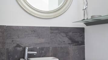 A bathroom with a toilet, a sink, a mirror, and a toilet paper holder.