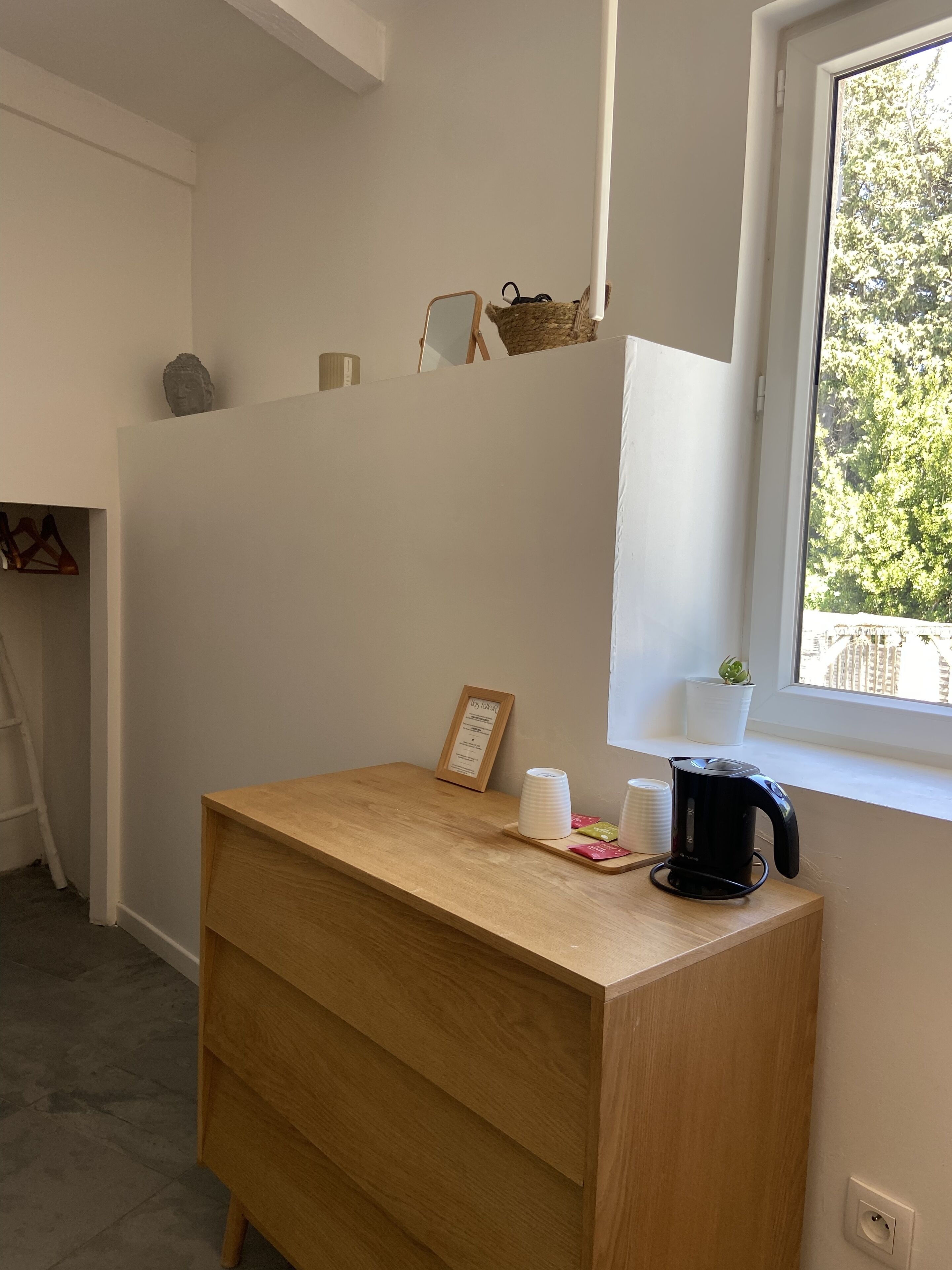 A wooden desk with a black kettle, a framed certificate, and stacked cups.