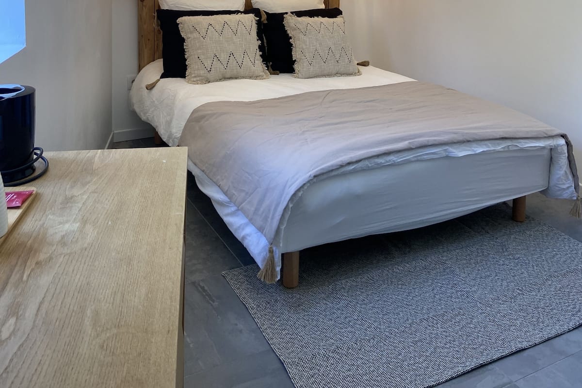 A bedroom with a wooden headboard, two hanging lamps, a bed with white bedding, and a small bedside table with a lamp.