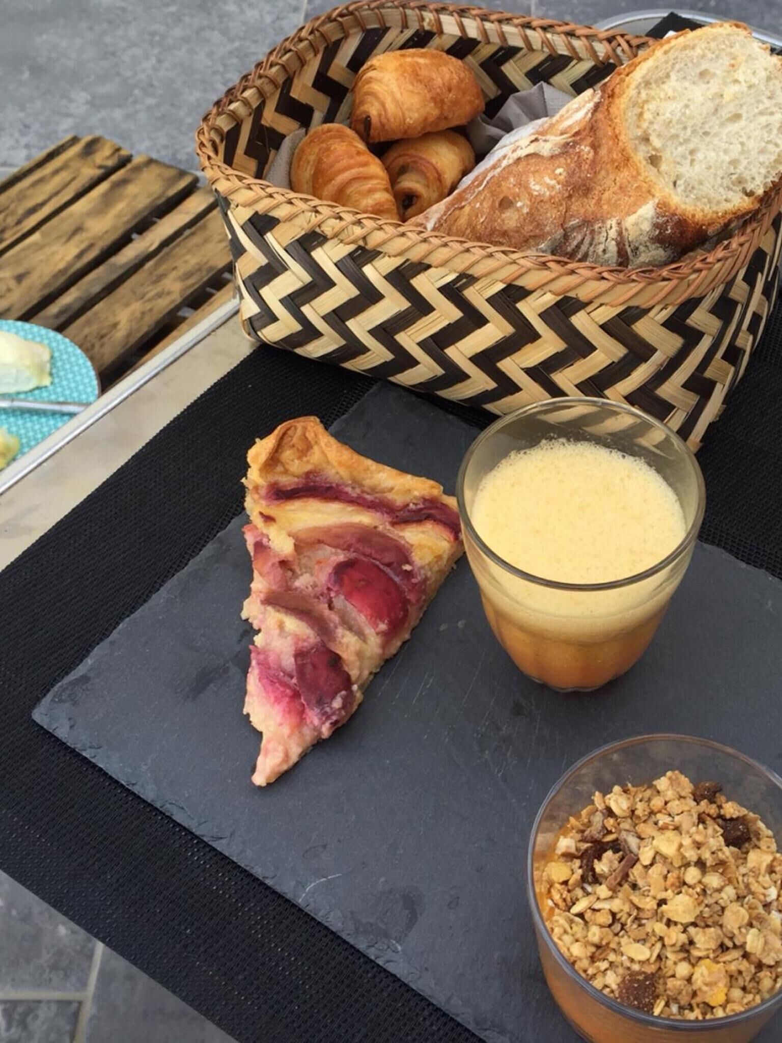 A table with a slice of pie, a glass of coffee, a basket of bread, and a bowl of granola.