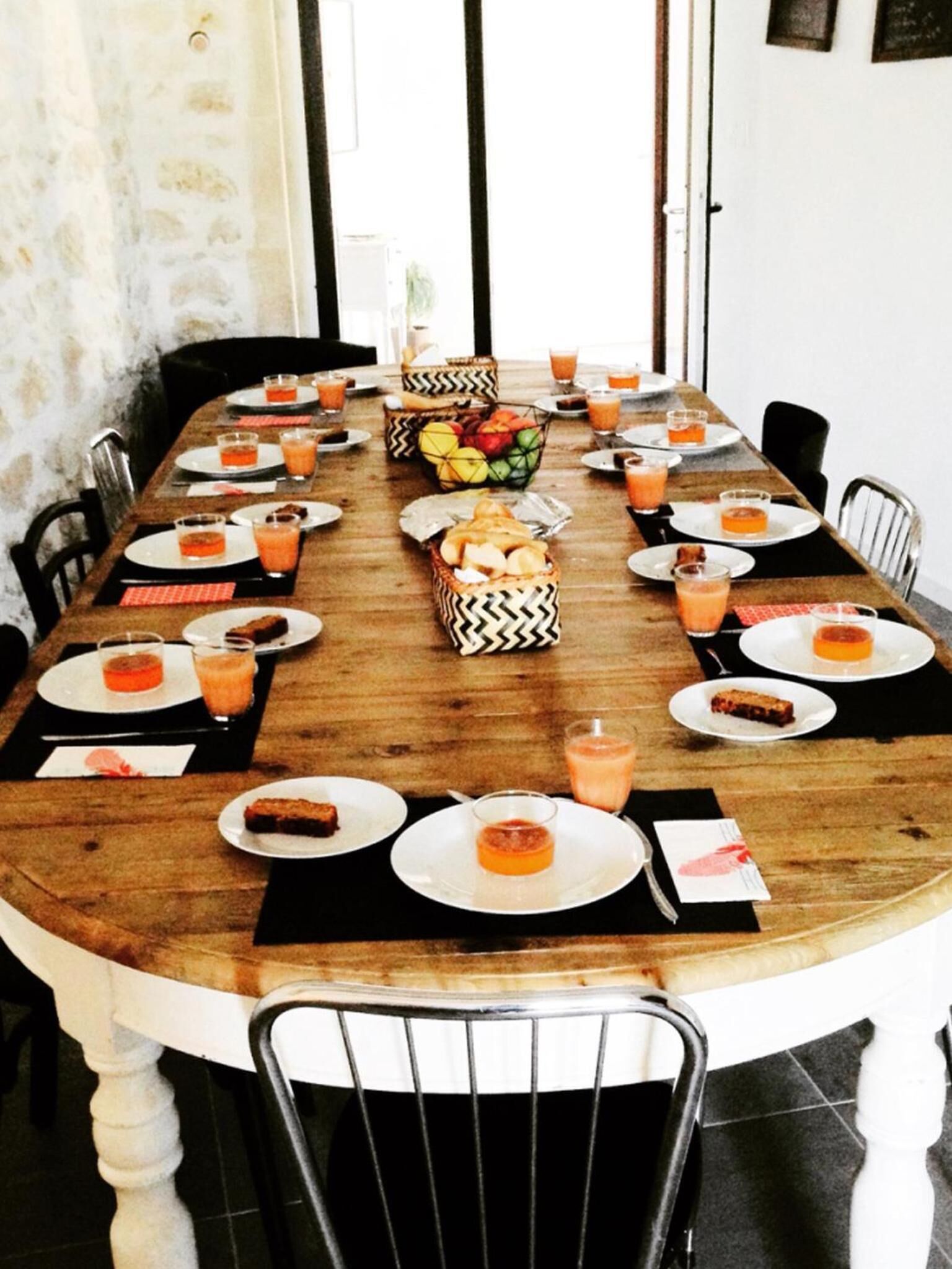 Een lange houten eettafel gedekt met borden, glazen en schalen vol fruit en gebak.