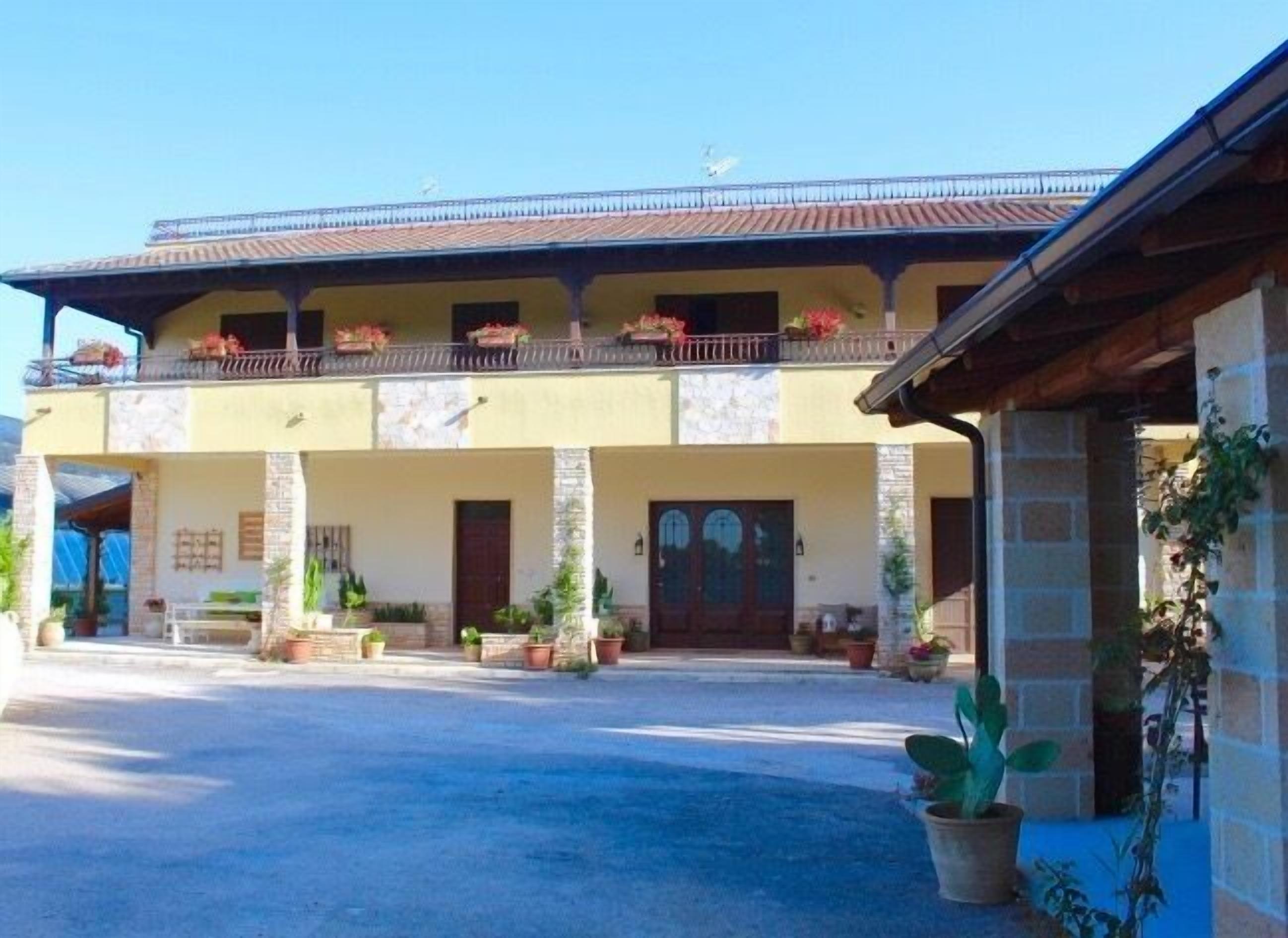 A two-story building with a balcony, potted plants, and a clear sky.