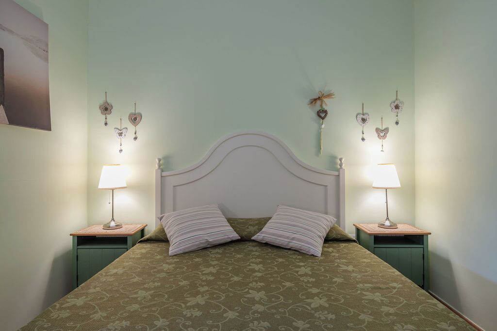 A neatly arranged bedroom with a bed centered between two nightstands, each with a lamp and a small table.