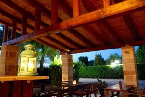 Un patio al aire libre con mesas y sillas de madera, un farolillo y un pilar de ladrillo.