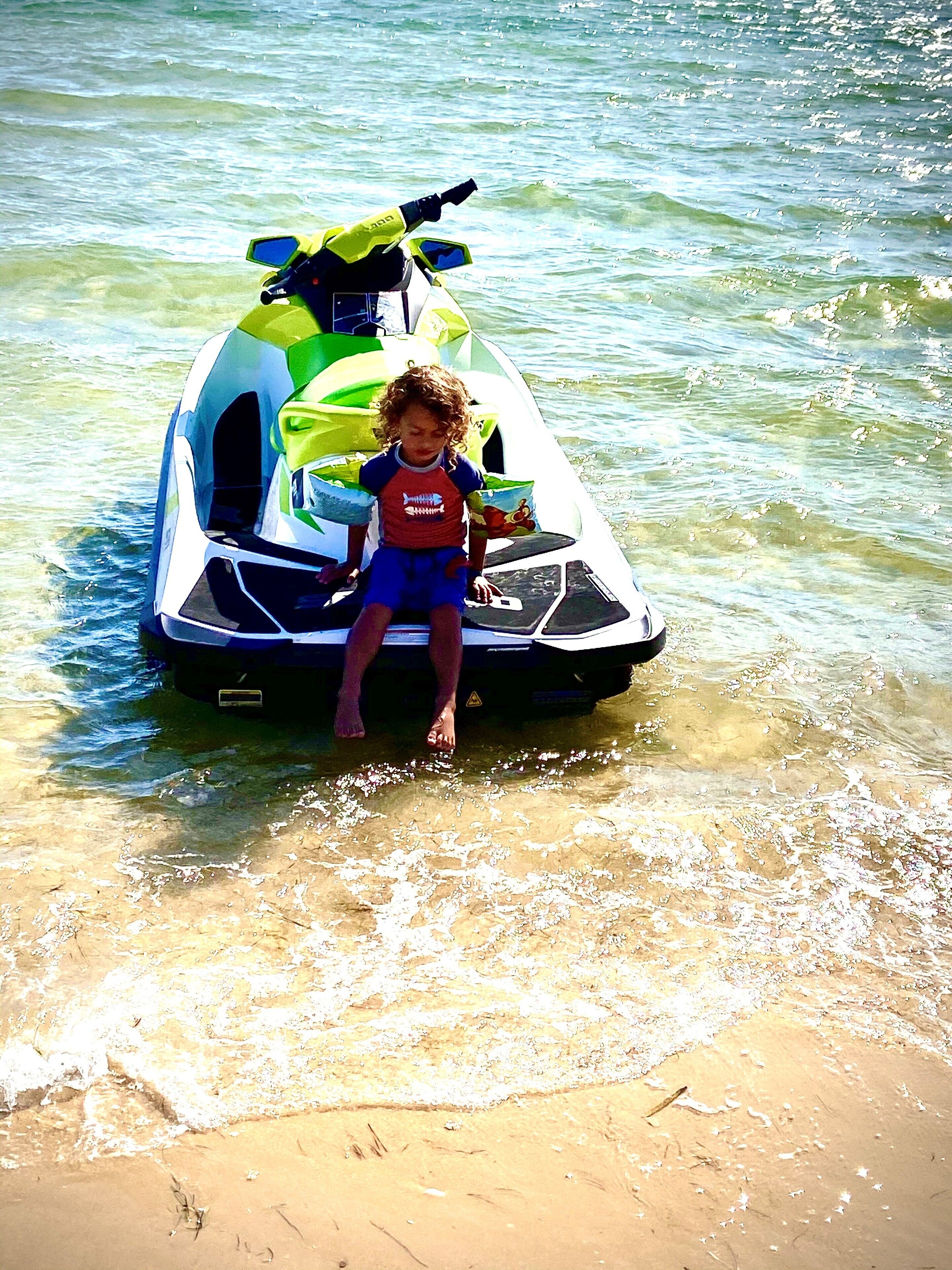 A child sitting on a jet ski in shallow water.
