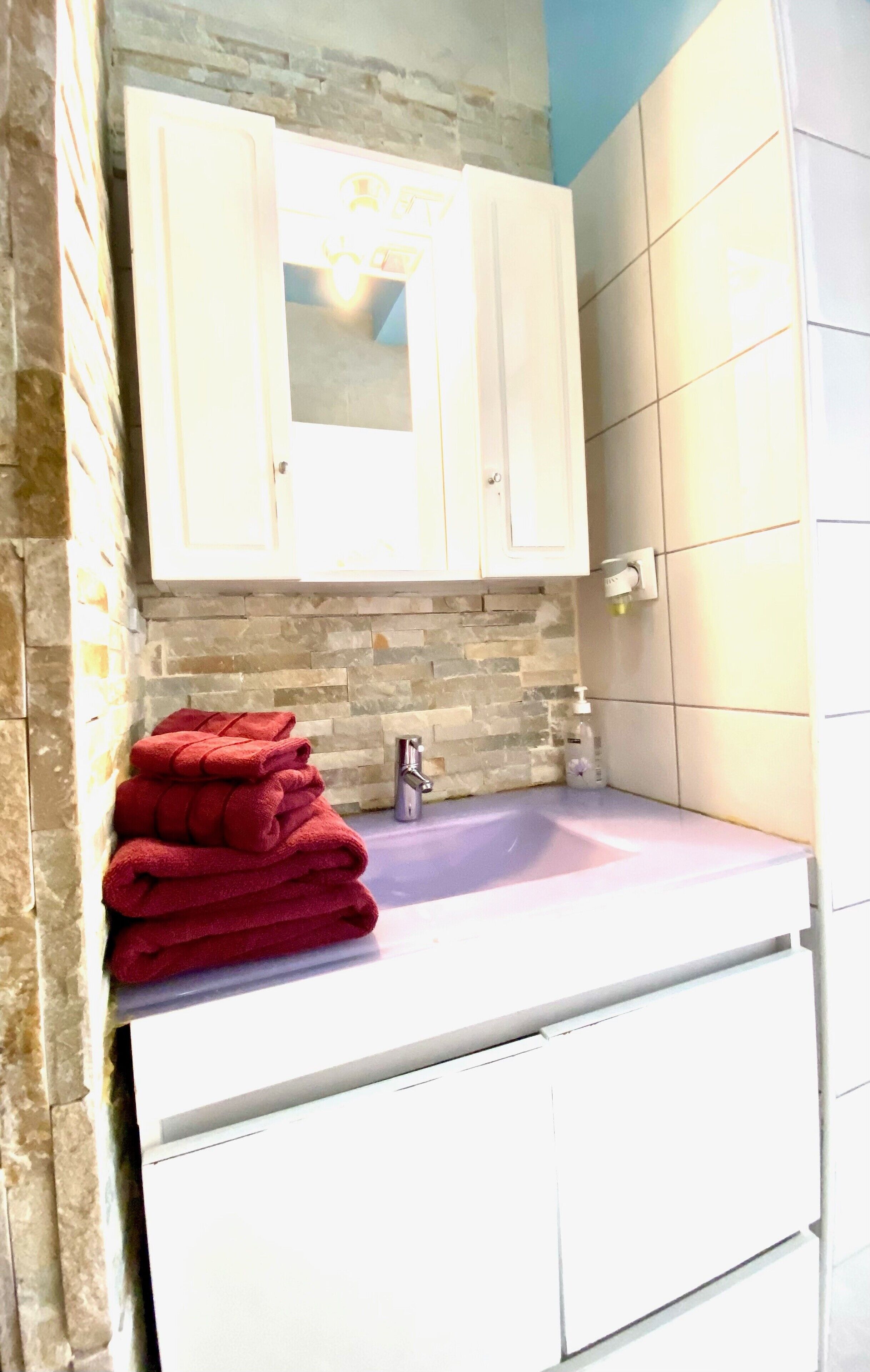 Un baño con salpicadero de piedra, armarios blancos y un lavamanos morado.