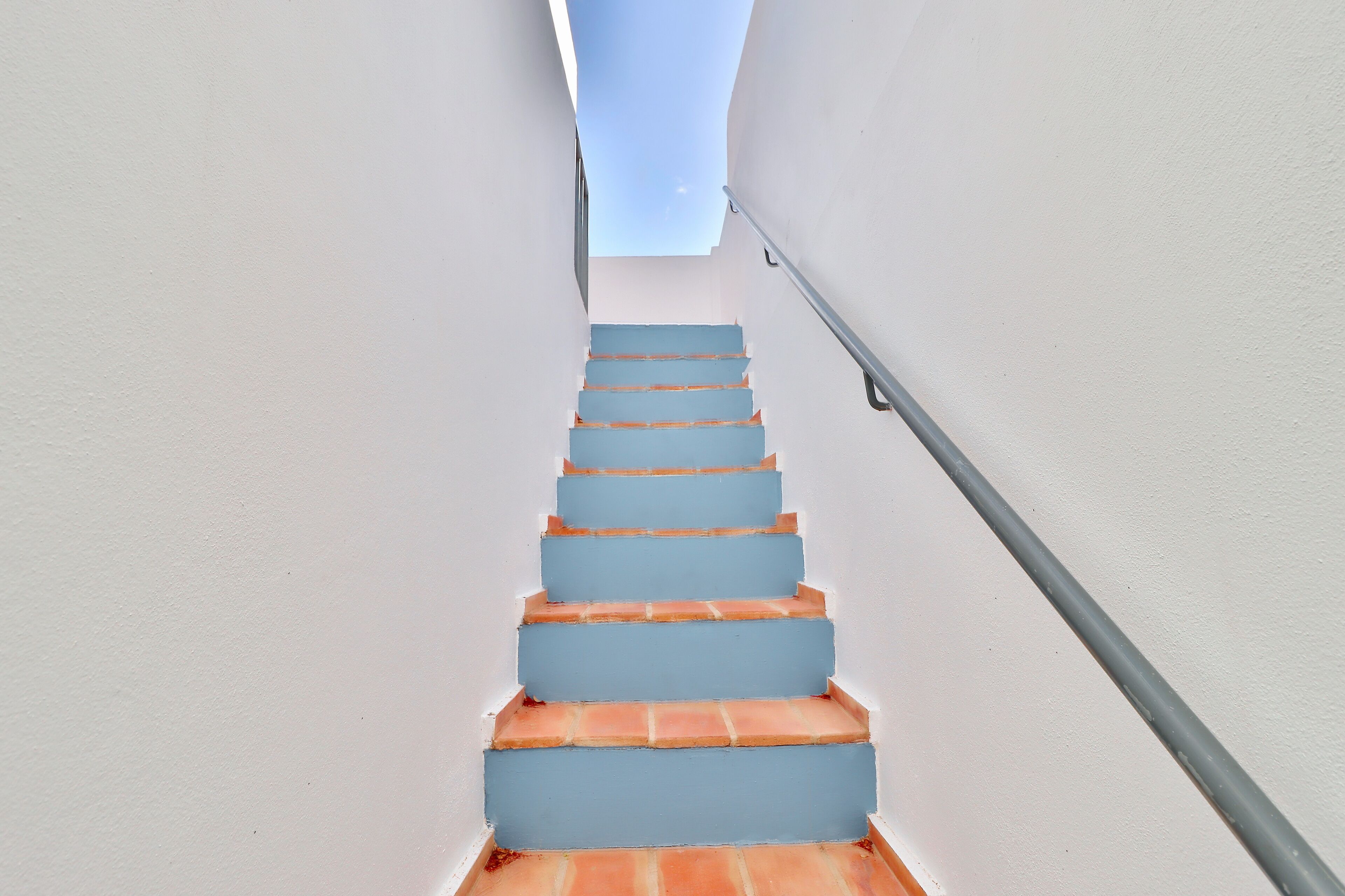 Una escalera con escalones azules que ascienden, rodeada de paredes blancas.