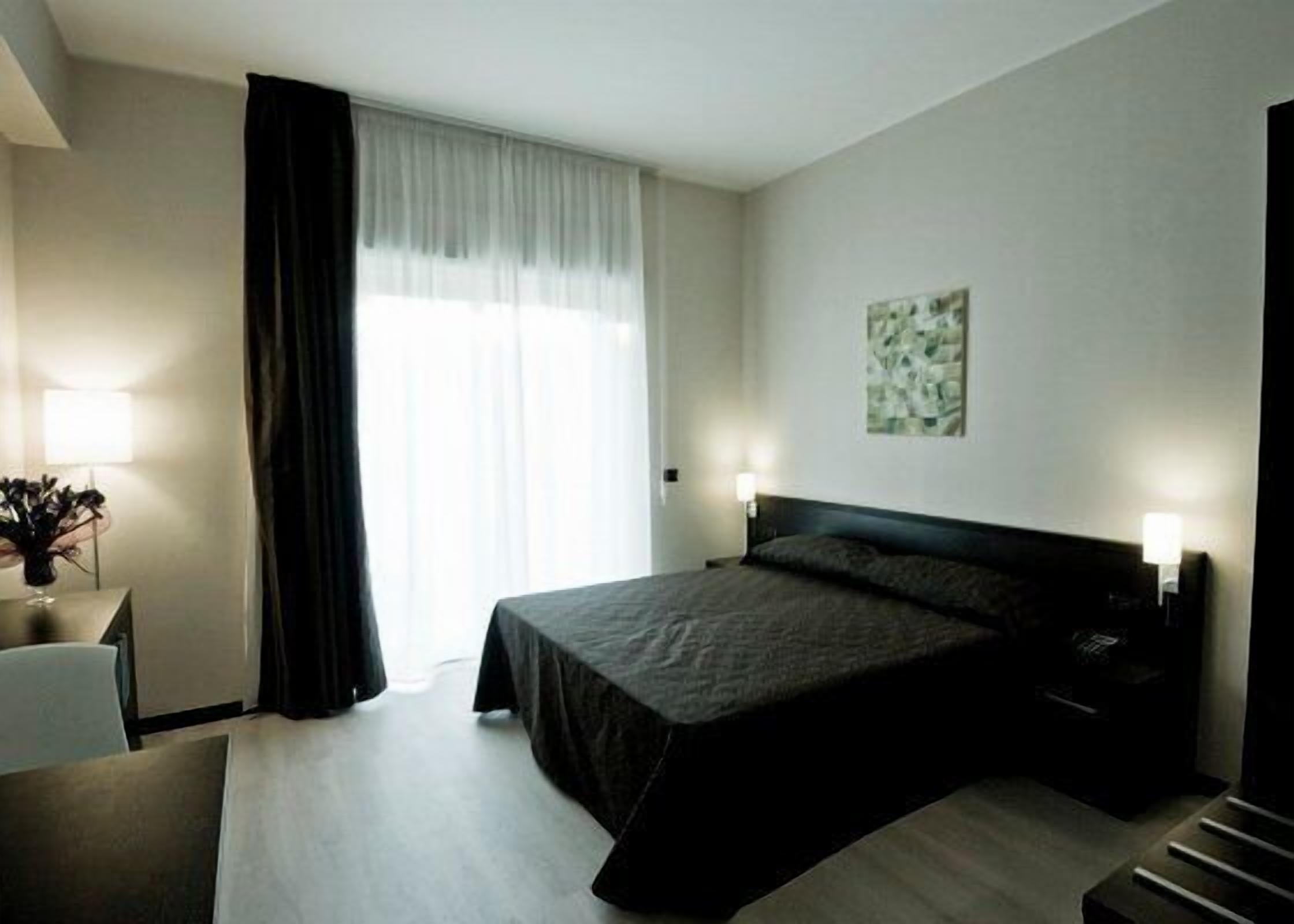 Habitación de hotel con una cama grande, un escritorio con lámpara y una ventana con cortinas.