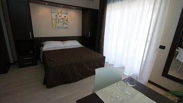 Ein modernes Hotelzimmer mit einem großen Bett, einem kleinen Tisch mit zwei Weingläsern und einem Gemälde an der Wand.
